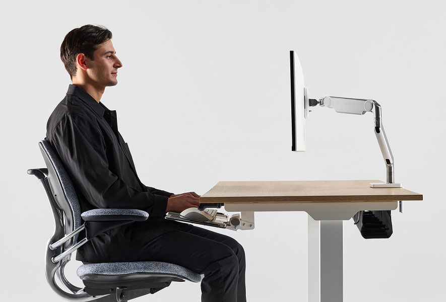Personne assise à un bureau eFloat Go 2.0, sur une chaise Freedom Task, tapant sur un clavier monté au bureau avec un M2 Pro